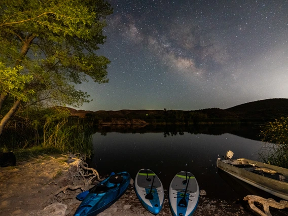 night photography of patagonia lake. Milky way can bee seen in the sky. Boats and canoes can be seen near the shore.