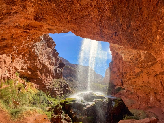 hole in red rock with water pouring down on a sunny day