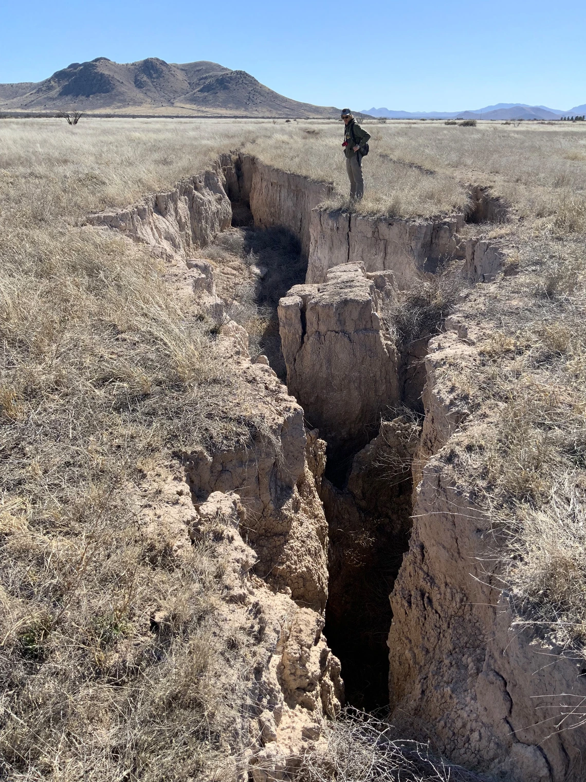 a photo of a man standing near a very large fissure. 30-40 feet long and quite deep