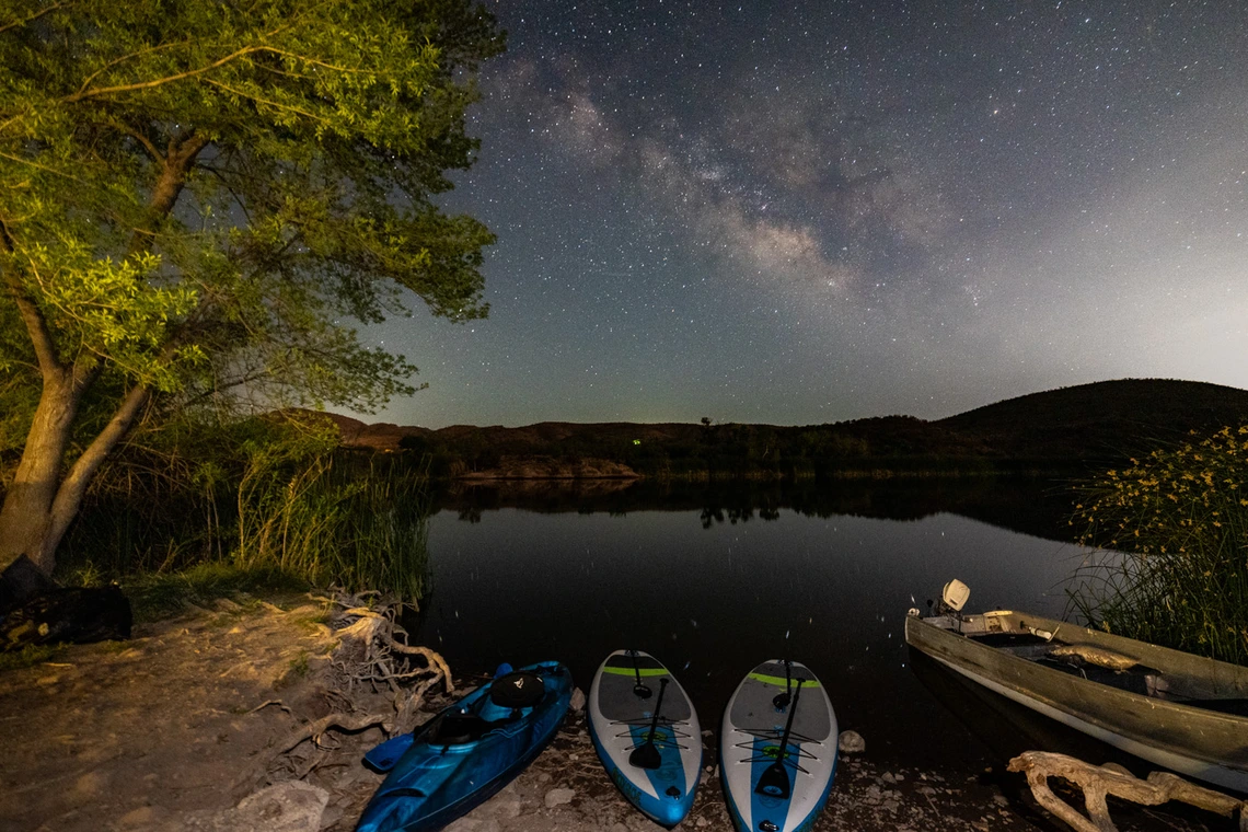 night photography of patagonia lake. Milky way can bee seen in the sky. Boats and canoes can be seen near the shore.