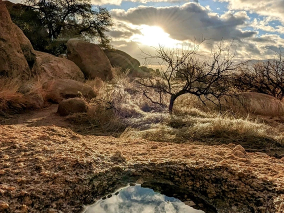 a photo featuring a small pool of water in a desert landscape with clouds and a blue sky