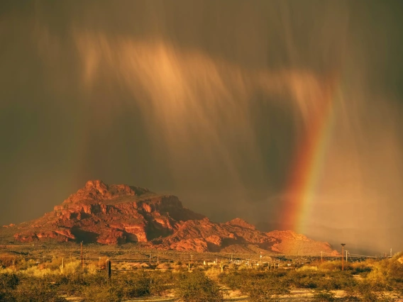 photo of a mountain with rain clouds and a rainbow with a reddish-brown cast