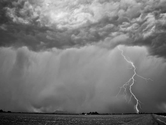 black and white photo showing an agricultural landscape with showing rain and a single lightning bolt