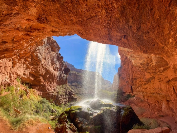 hole in red rock with water pouring down on a sunny day