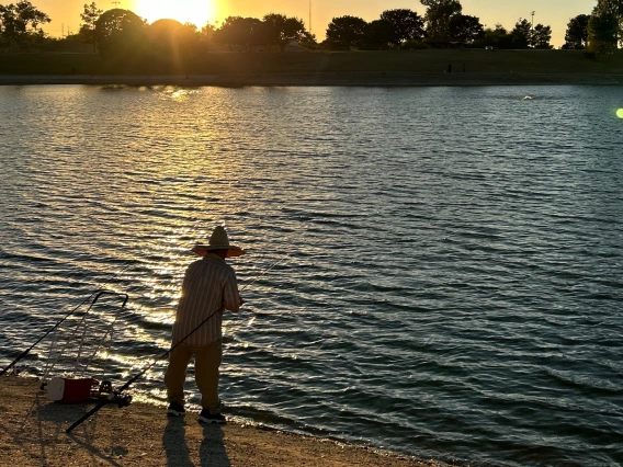 photo showing a person fishing on the edge of a lake at sunset