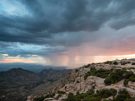 photo of a group of people in a rocky terrain with rain and a pretty sky with clouds, blues and pinks