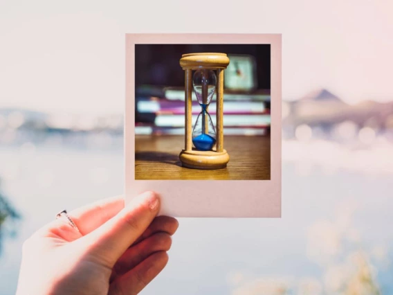 a hand holding a Polaroid image of an hourglass