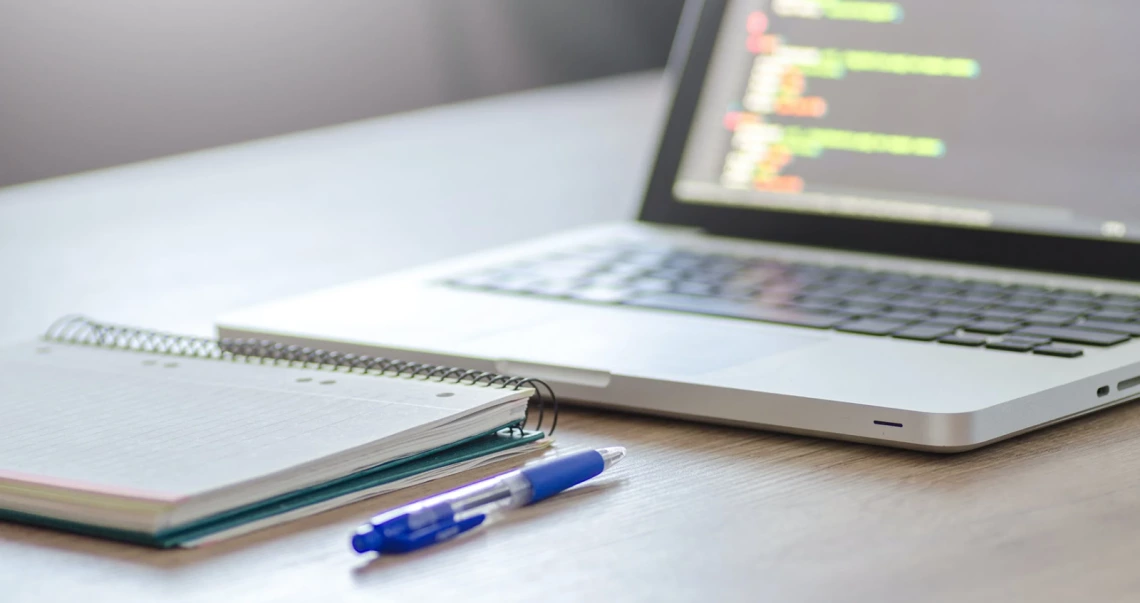 stock photo of a laptop with a note page and pen next to it.