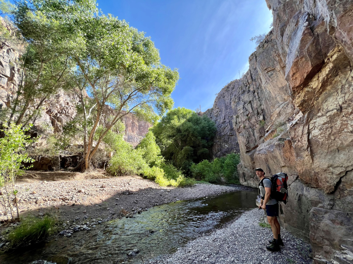 Nathan Nutter photo showing Aravaipa Canyon on a sunny day. A hiker is shown standing next to aravaipa creekker is standing next to 