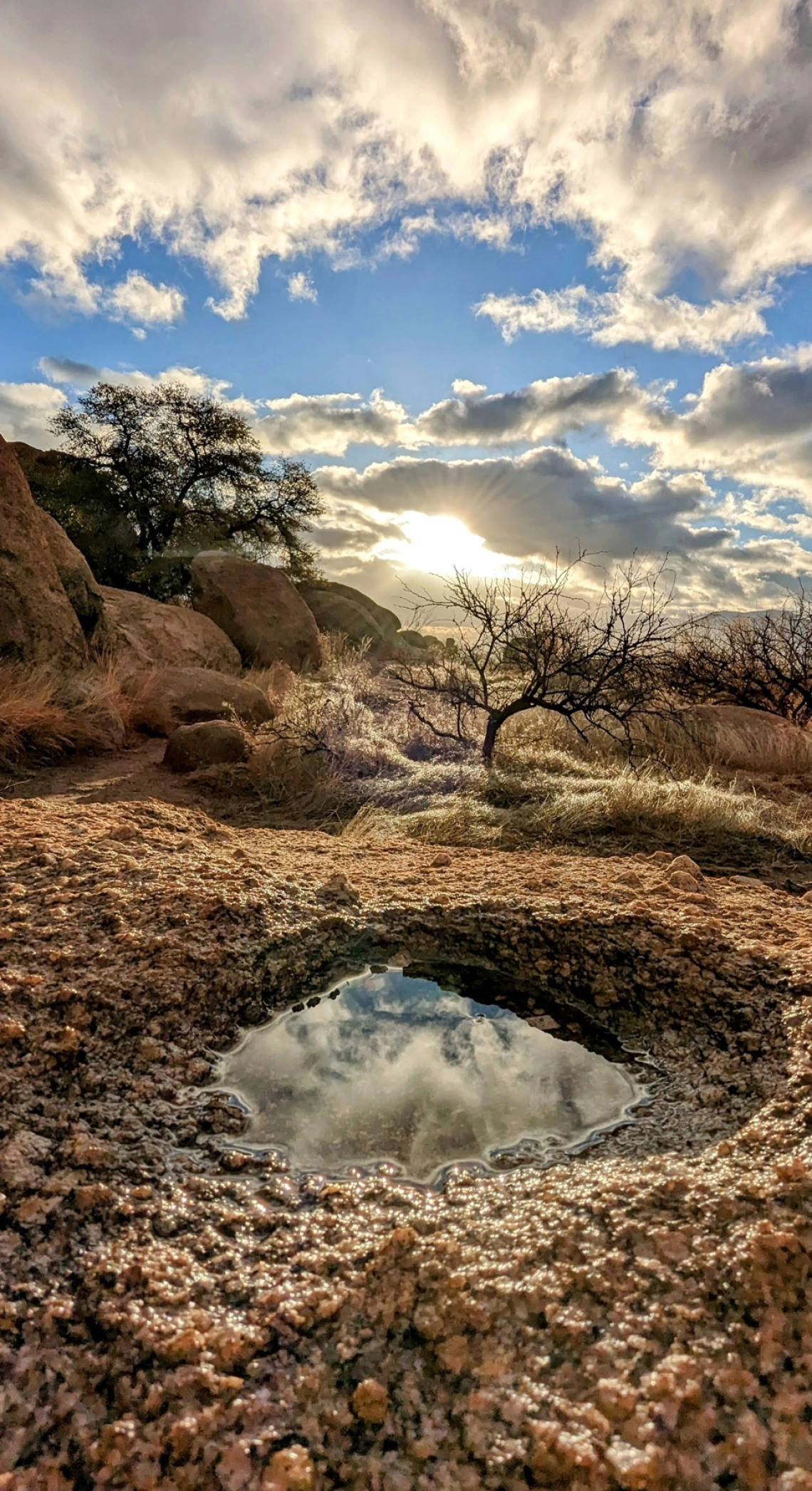 a photo featuring a small pool of water in a desert landscape with clouds and a blue sky