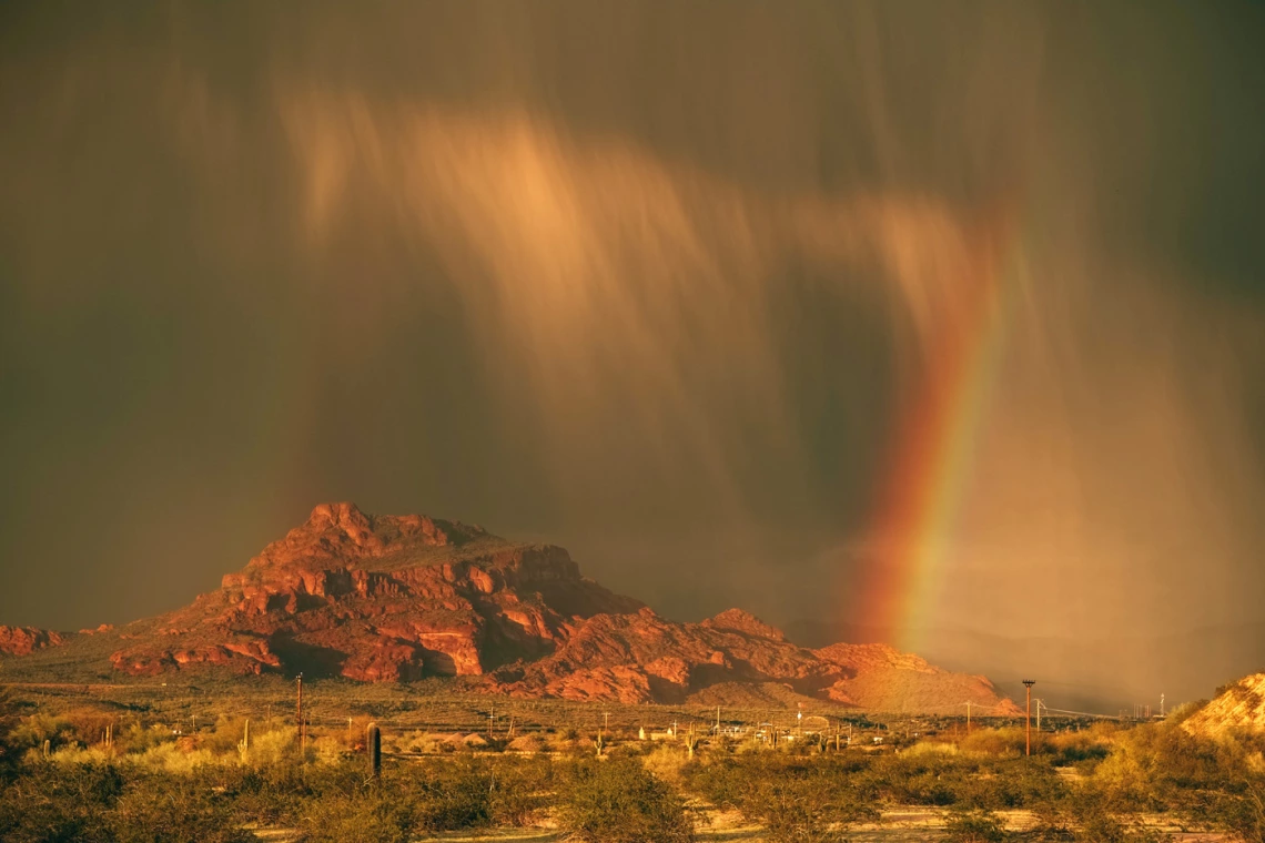 photo of a mountain with rain clouds and a rainbow with a reddish-brown cast