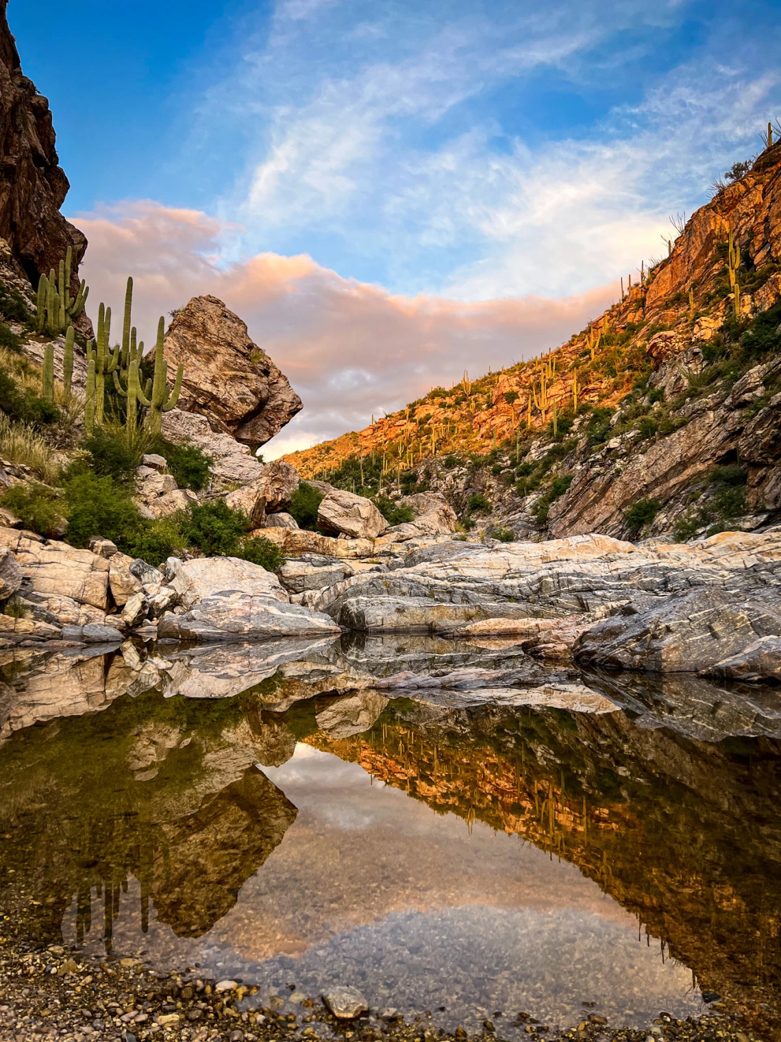 photo showing a pool in a desert setting with a reflection. clouds and blue sky.