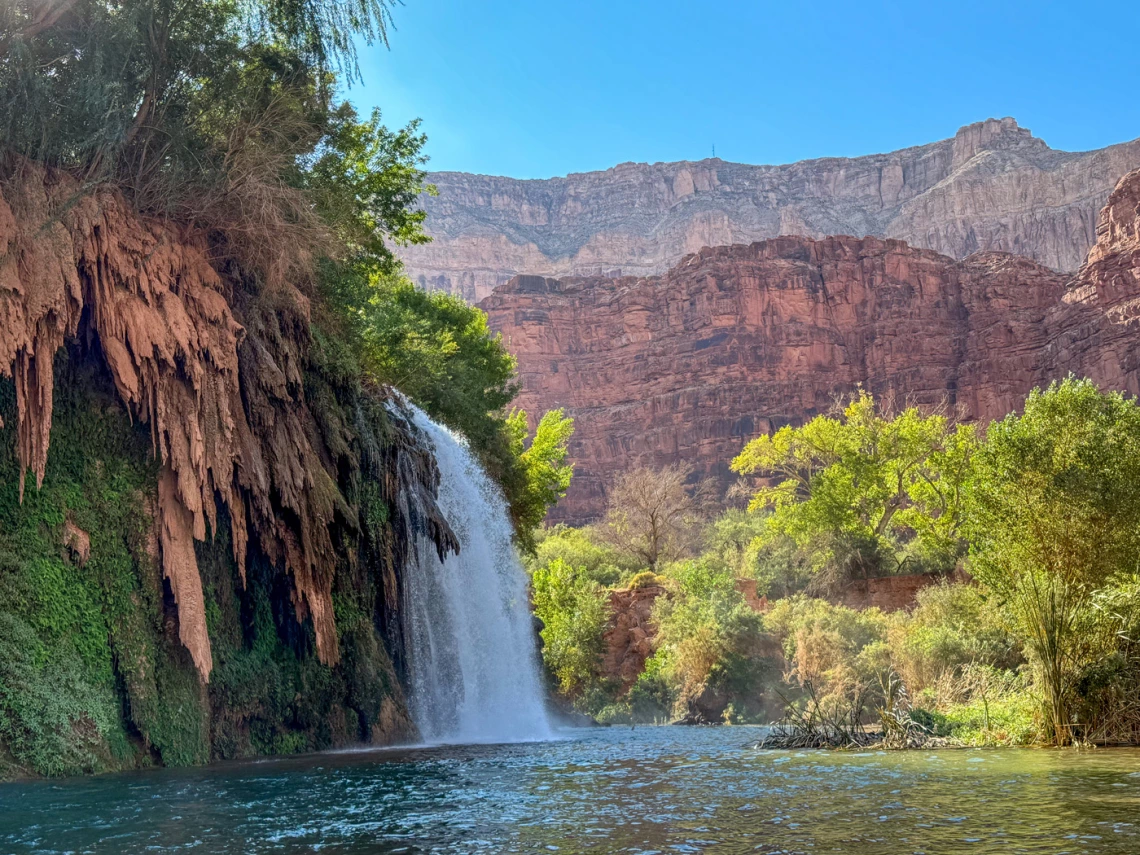 a photo of a small waterfall with red rock cliffs and trees in the background