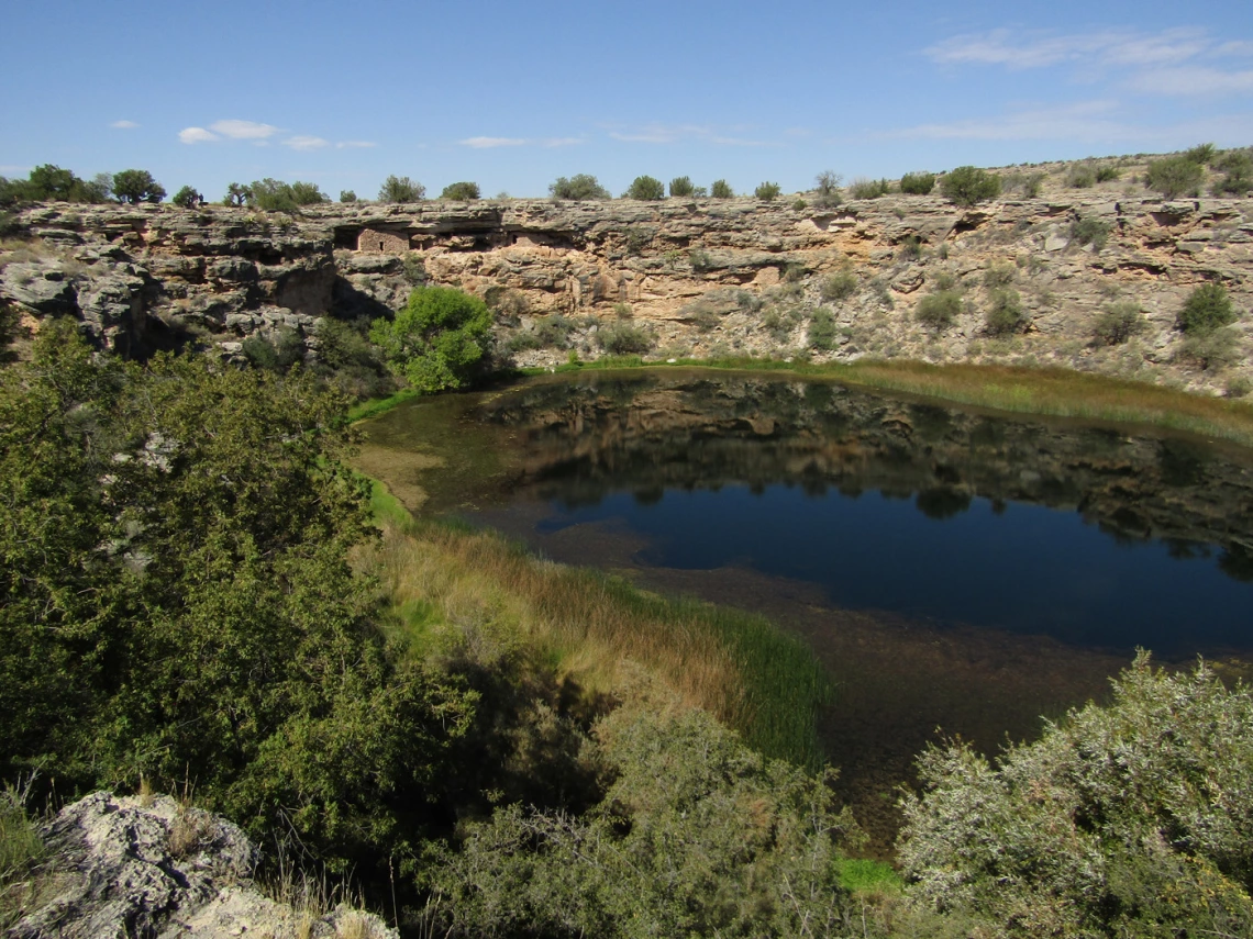 a photo of Montezuma Well showing a pool of water with a reflection surrounded by desert plant life