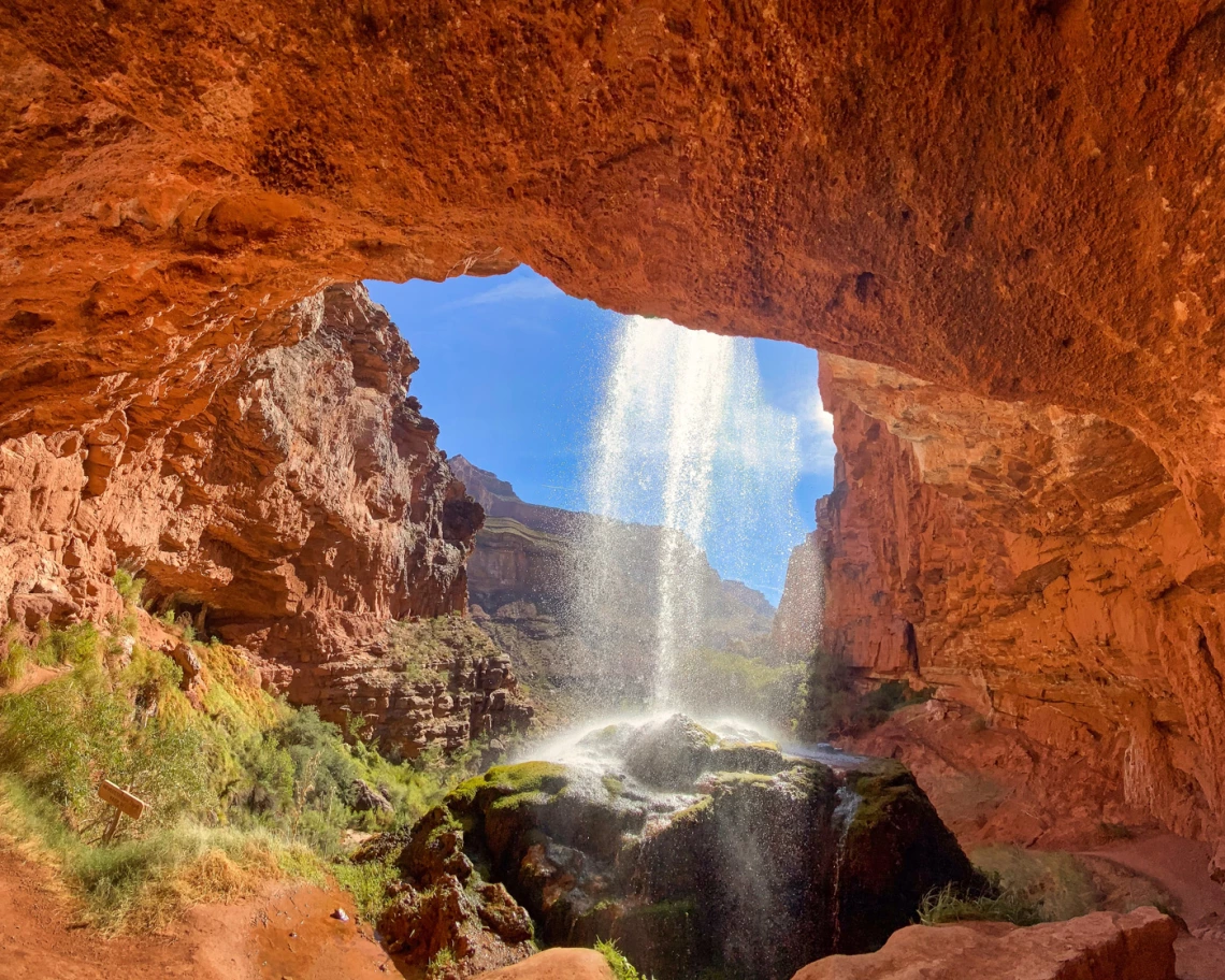 hole in red rock with water pouring down on a sunny day