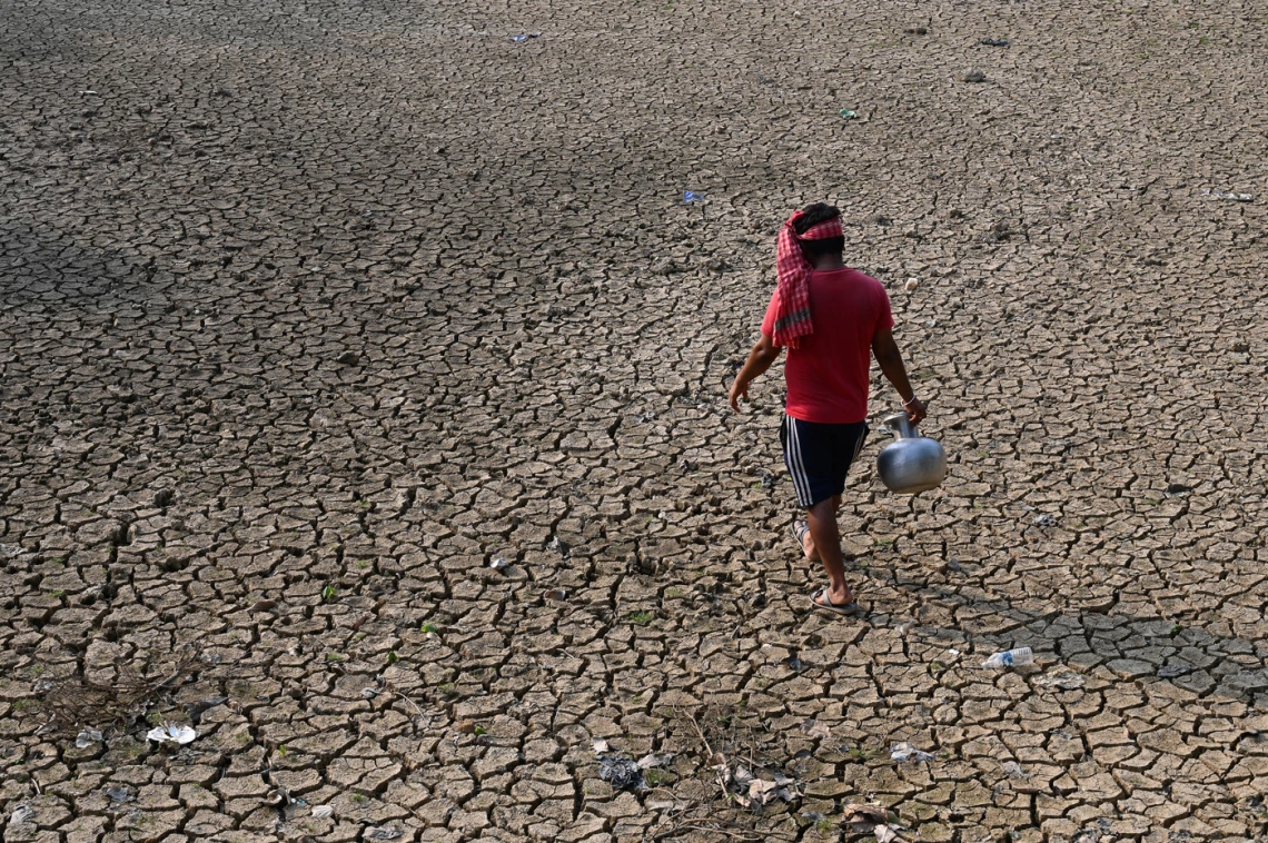 photo of a person walking on cracked earth with a water vessel in their hand 