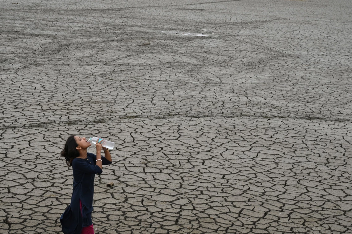 photo of a person drinking water on cracked earth landscape