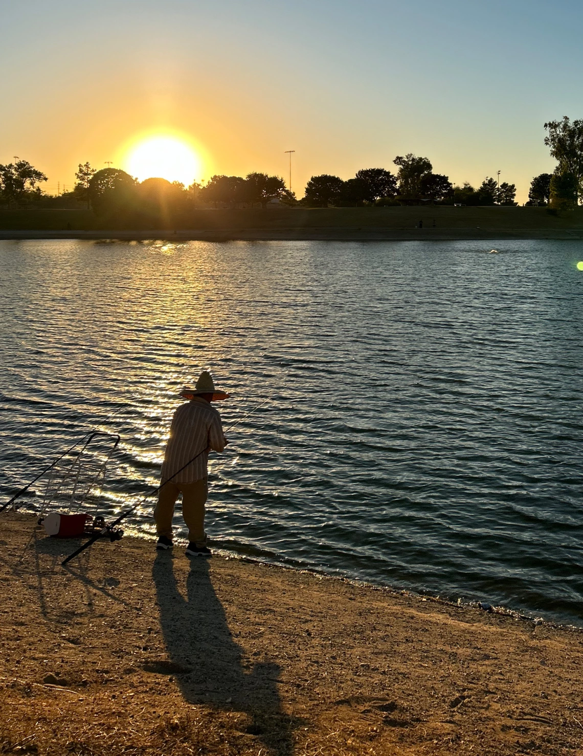 photo showing a person fishing on the edge of a lake at sunset