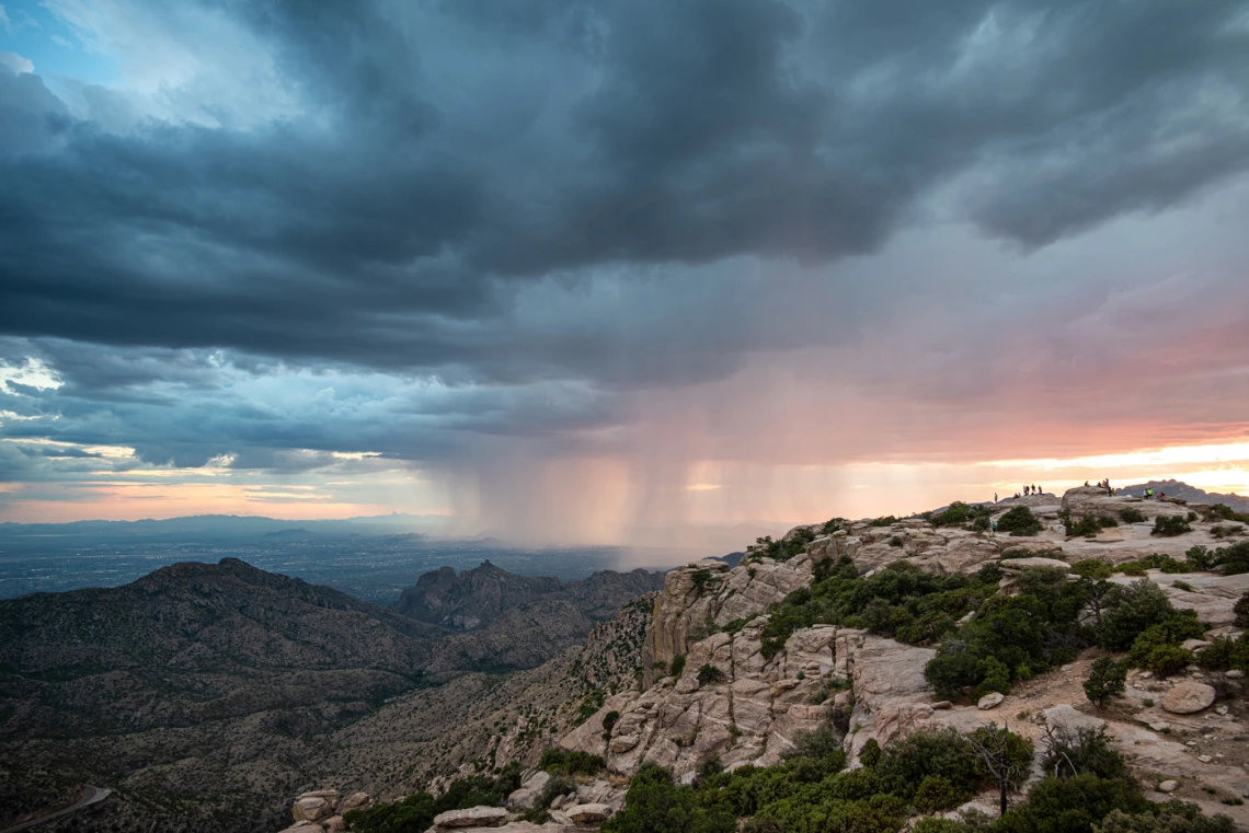 photo of a group of people in a rocky terrain with rain and a pretty sky with clouds, blues and pinks