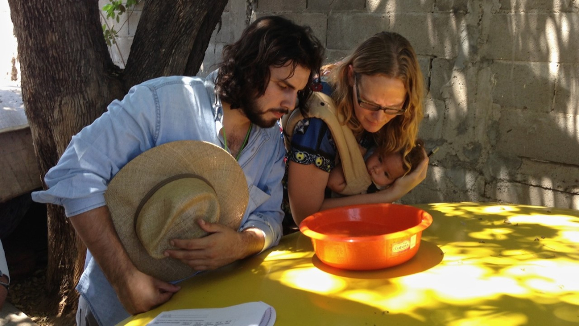 An image of a man and woman (holding a child) looking into a bowl of water