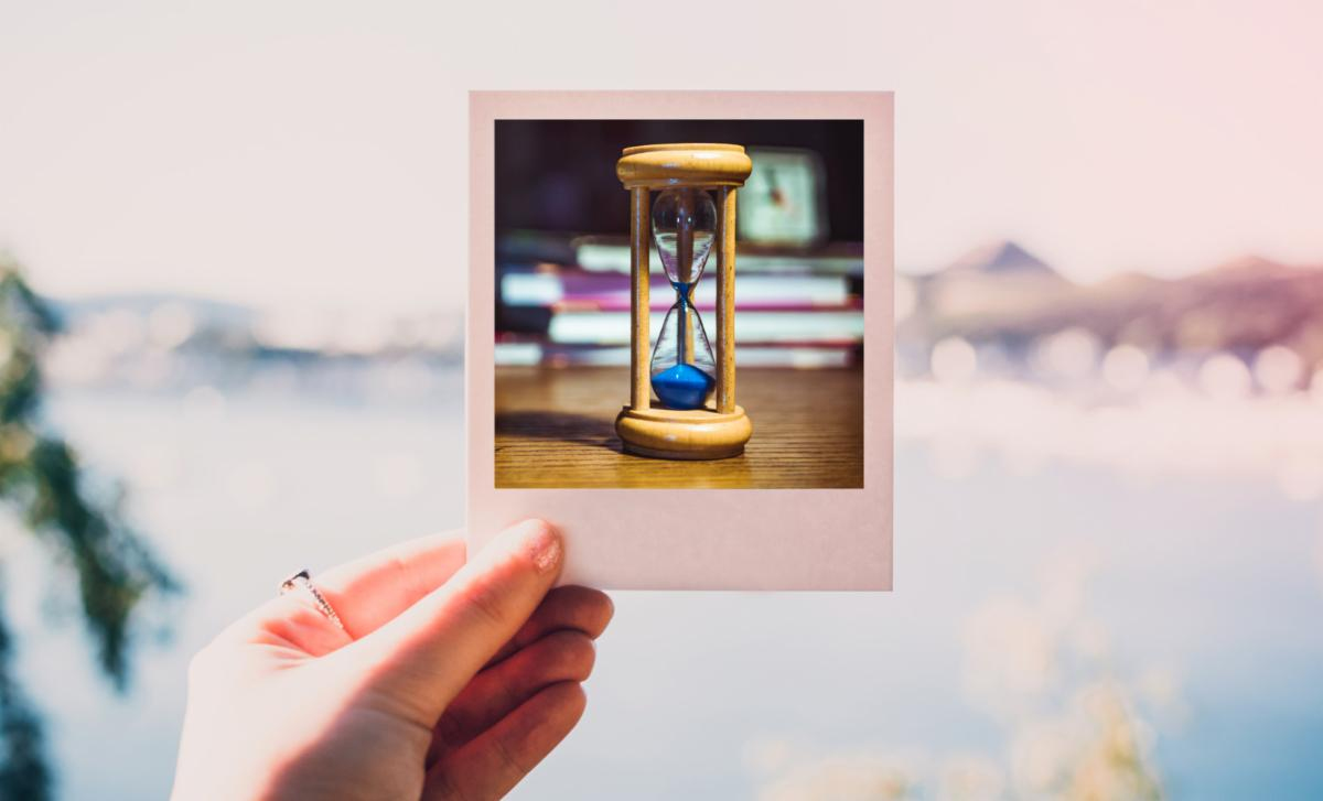 a hand holding a Polaroid image of an hourglass