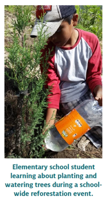 Elementary school student learning about plants and watering trees during a school-wide reforestation event